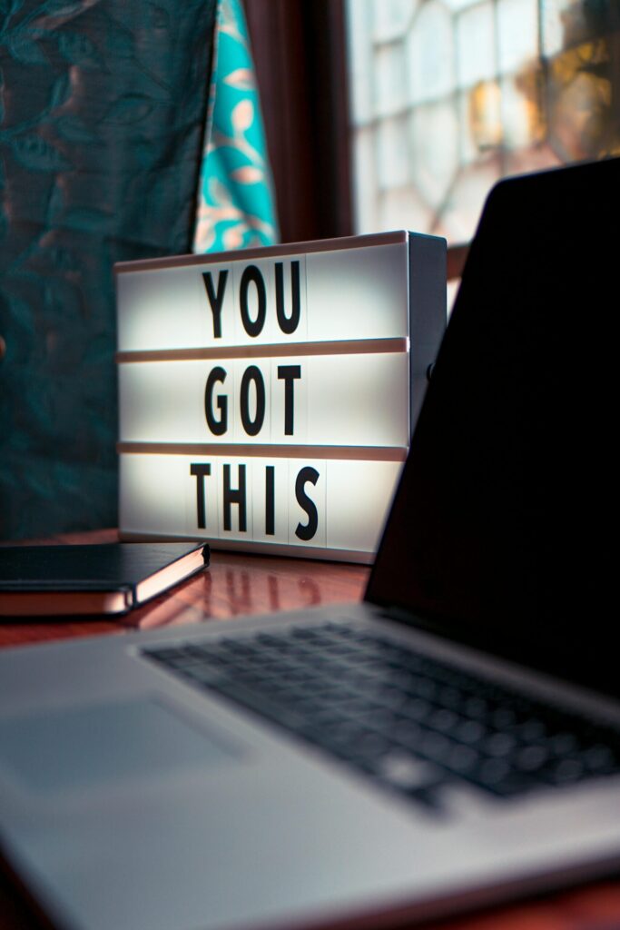 pexels-photo-2740954-2740954 Illuminated lightbox with a motivational quote beside a laptop, promoting productivity.