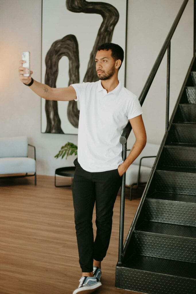 pexels-photo-31207780-31207780 Man in casual attire taking a selfie in a modern indoor setting with abstract art.