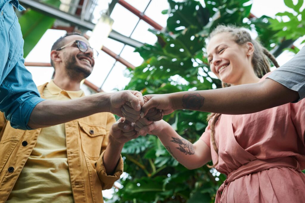 pexels-photo-3228684-3228684 A group of young adults celebrating teamwork with a fist bump in a lush outdoor setting.
