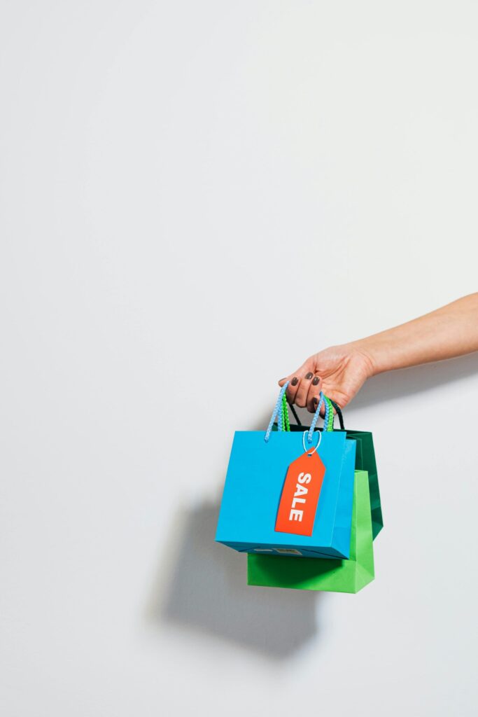 pexels-photo-5650019-5650019 A hand holding colorful shopping bags with a prominent sale tag, conveying a retail discount theme.