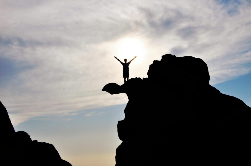 pexels-photo-584179-584179 Silhouette of a person celebrating on a mountain peak against a dramatic sky, symbolizing freedom and success.