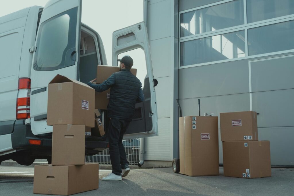 pexels-photo-6169056-6169056 A delivery man unloading cardboard boxes from a van at a warehouse during the day.